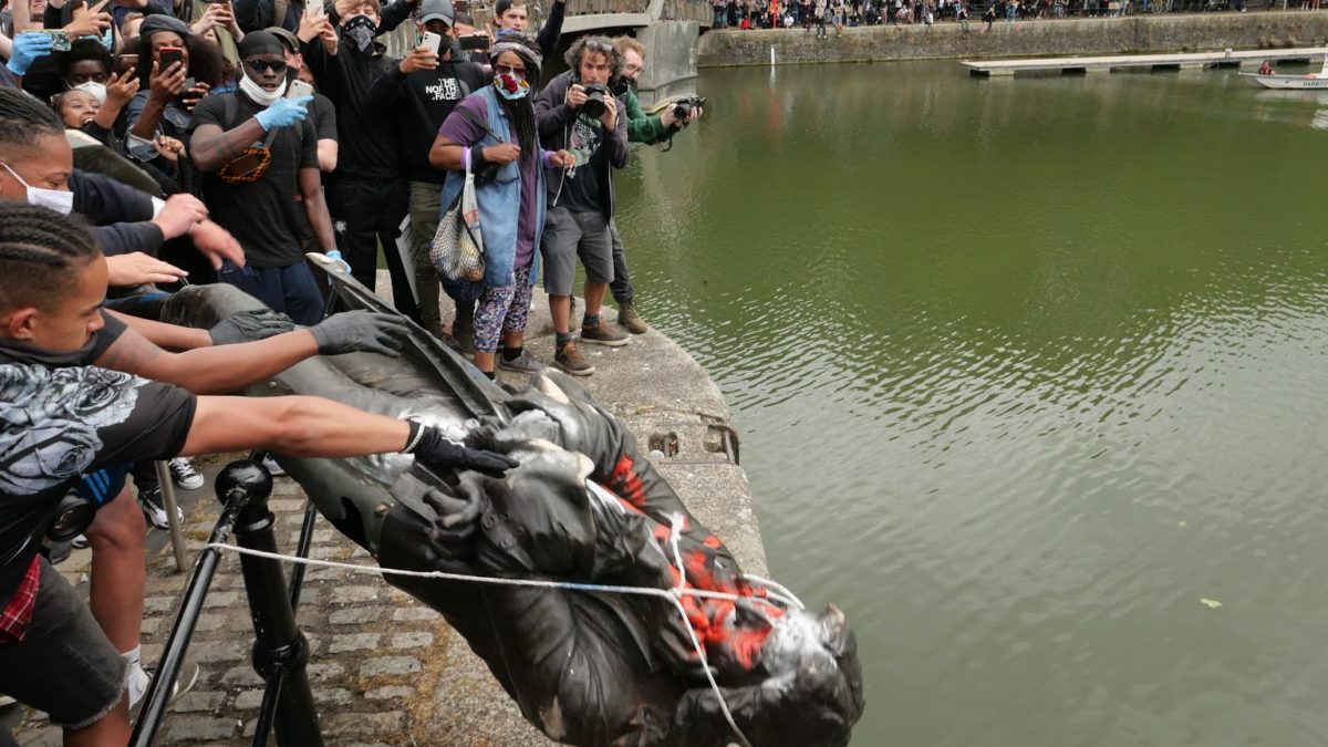 Photo: Crowds gather around the Floating Harbour and stand on Pero's Bridge as the statue of Edward Colston, covered in graffiti and with a rope around its neck is lifted over a fence to be thrown in to the water below.
