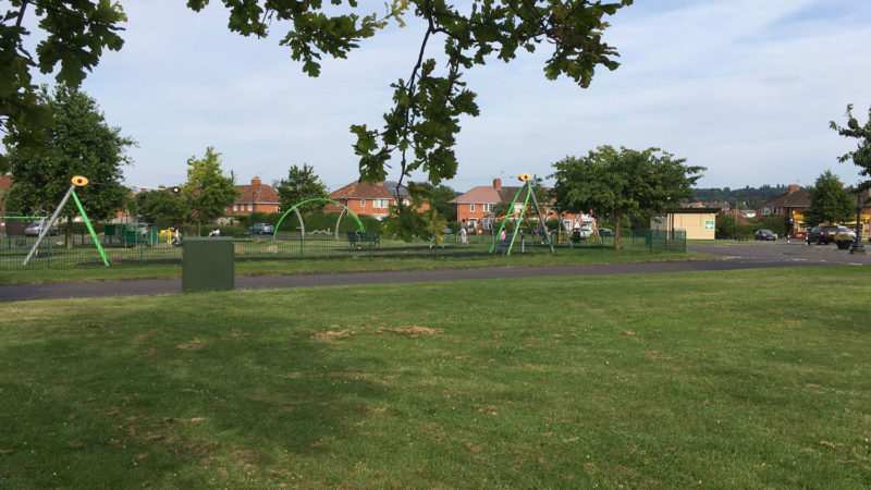 Green space with a children's playground and cafe in the background