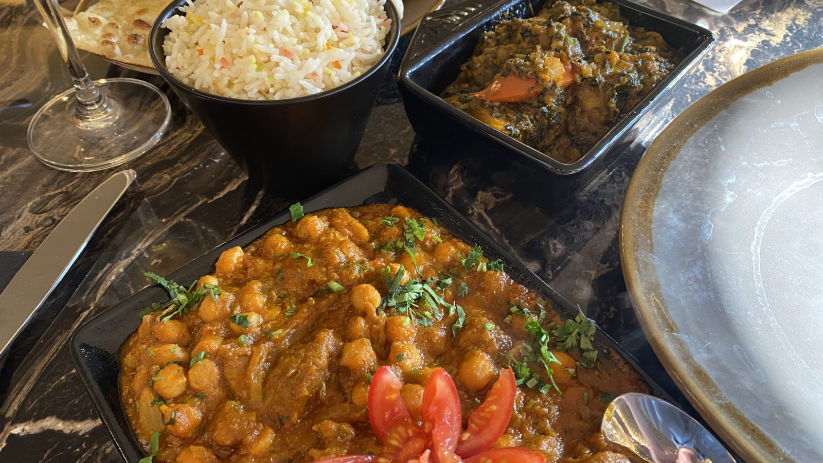 A plate of Afghan lamb curry in the foreground, with rice and saag aloo behind.
