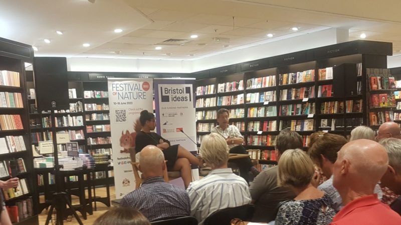 A seated crowd watch two people speak. 