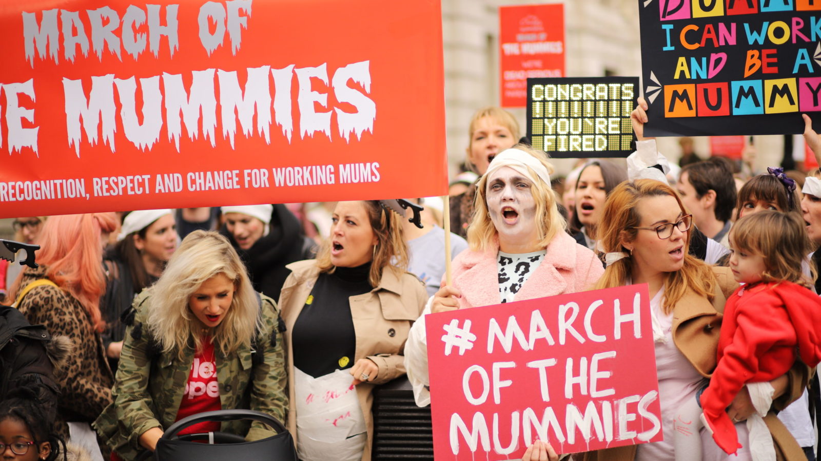 A crowd of protesters dressed in Halloween gear and holding banners that read #March of the Mummies.