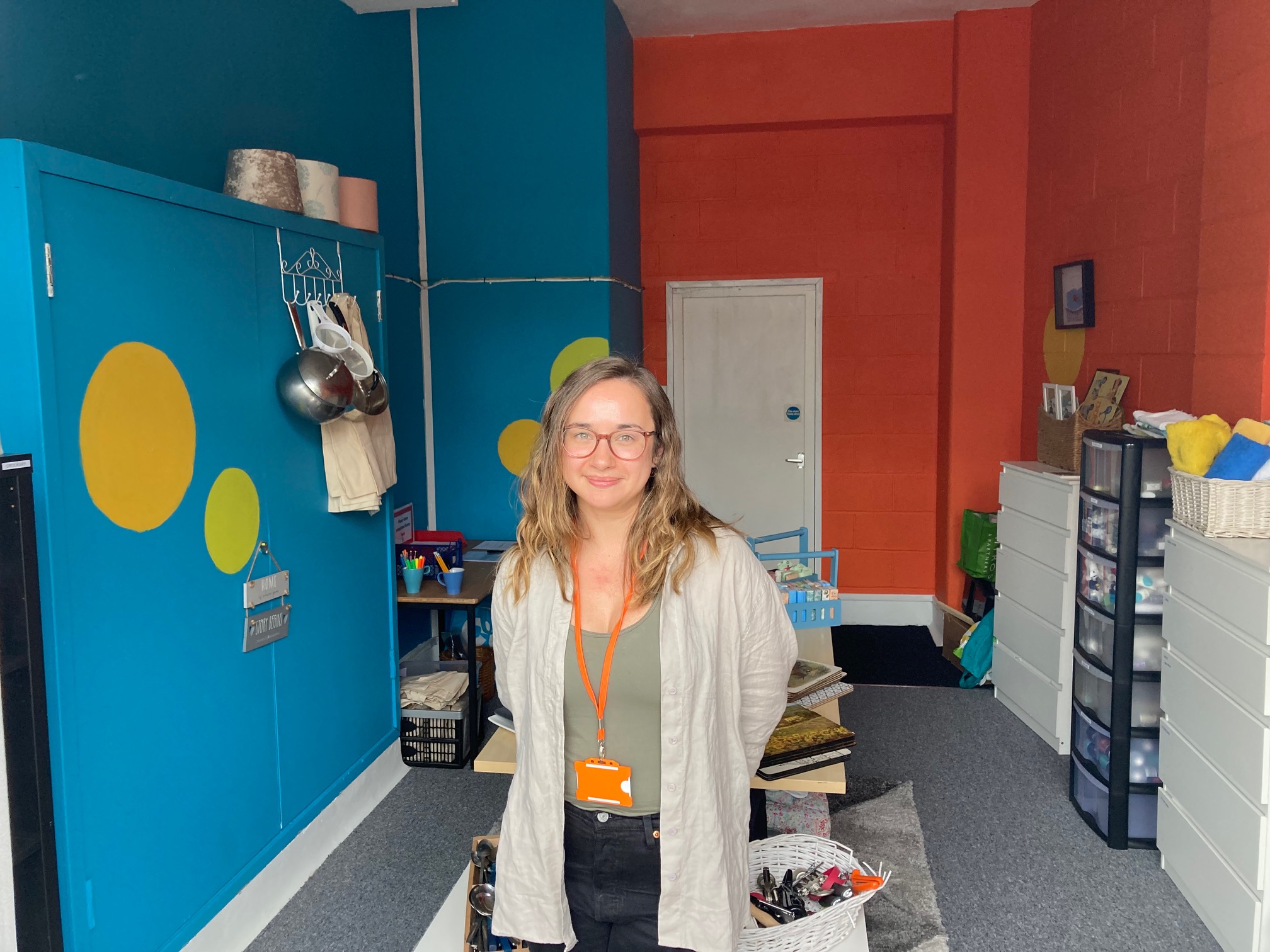A young woman stood smiling inside of a small, colourful shop