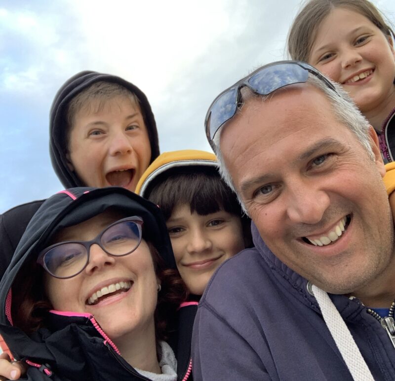 A family selfie, Lucy and her husband smile at the front of the group, with four children standing behind them also smiling. They are wrapped up warm.