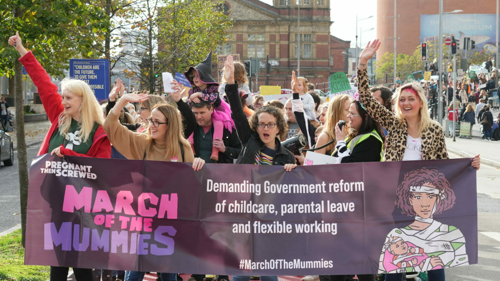 A crowd of parents holding a sign up at a protest against the cost of childcare crisis