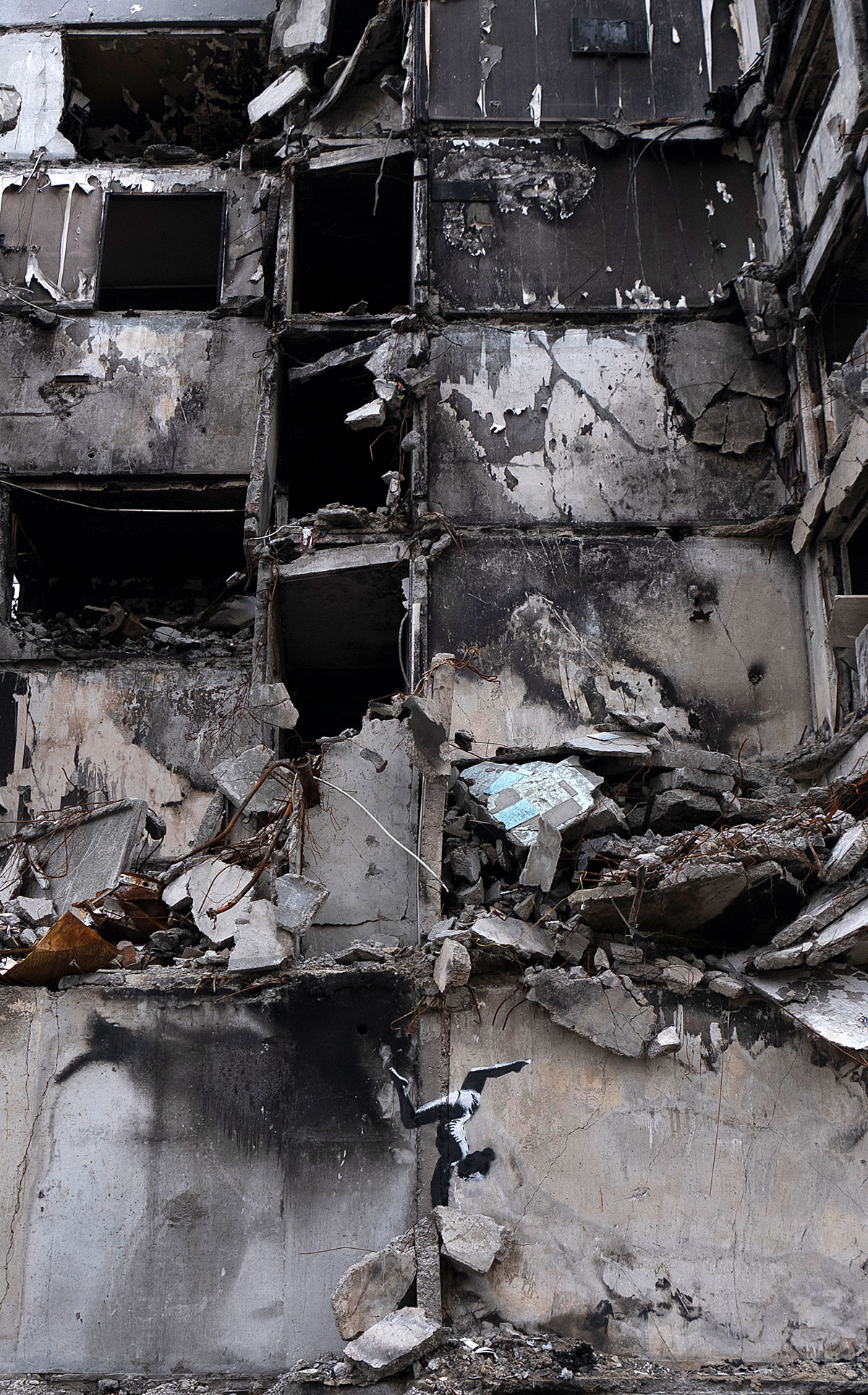 A building almost completely destroyed by shelling, with the stencil of a gymnast doing a handstand above some rubble on the ground floor