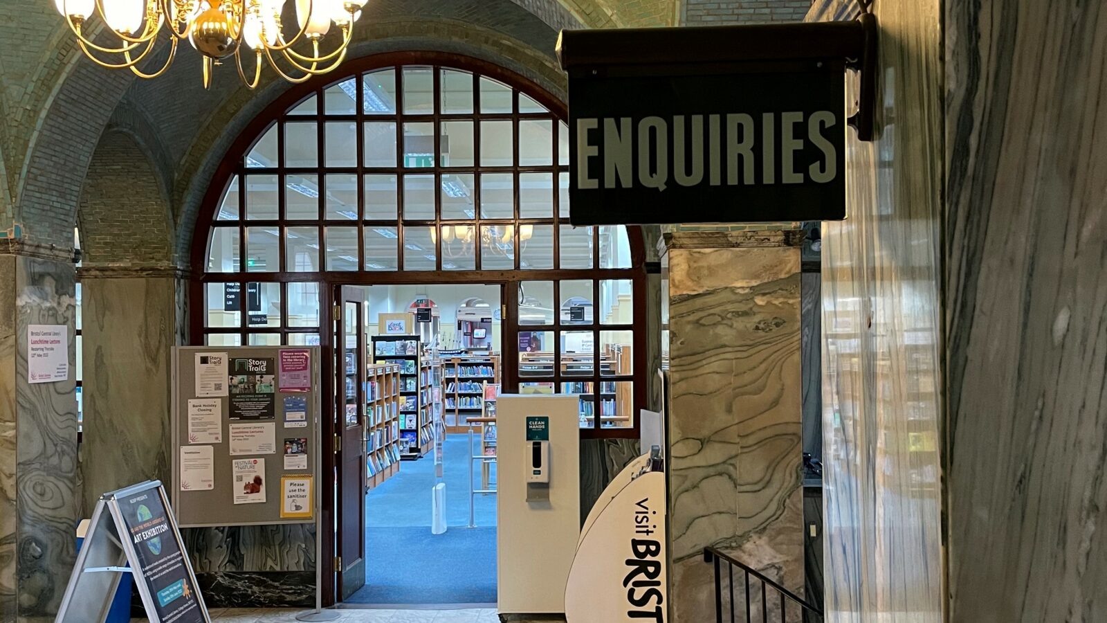A sign saying enquiries in the entrance area of Central Library with books seen through the entrance