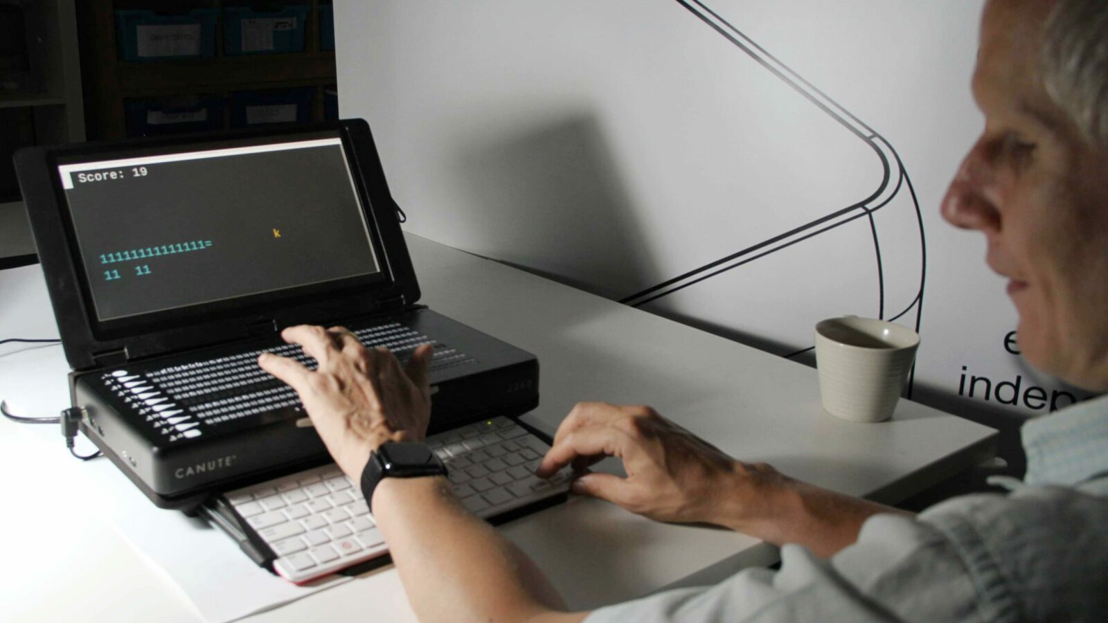 a man sat at a desk playing a braille video game at a laptop