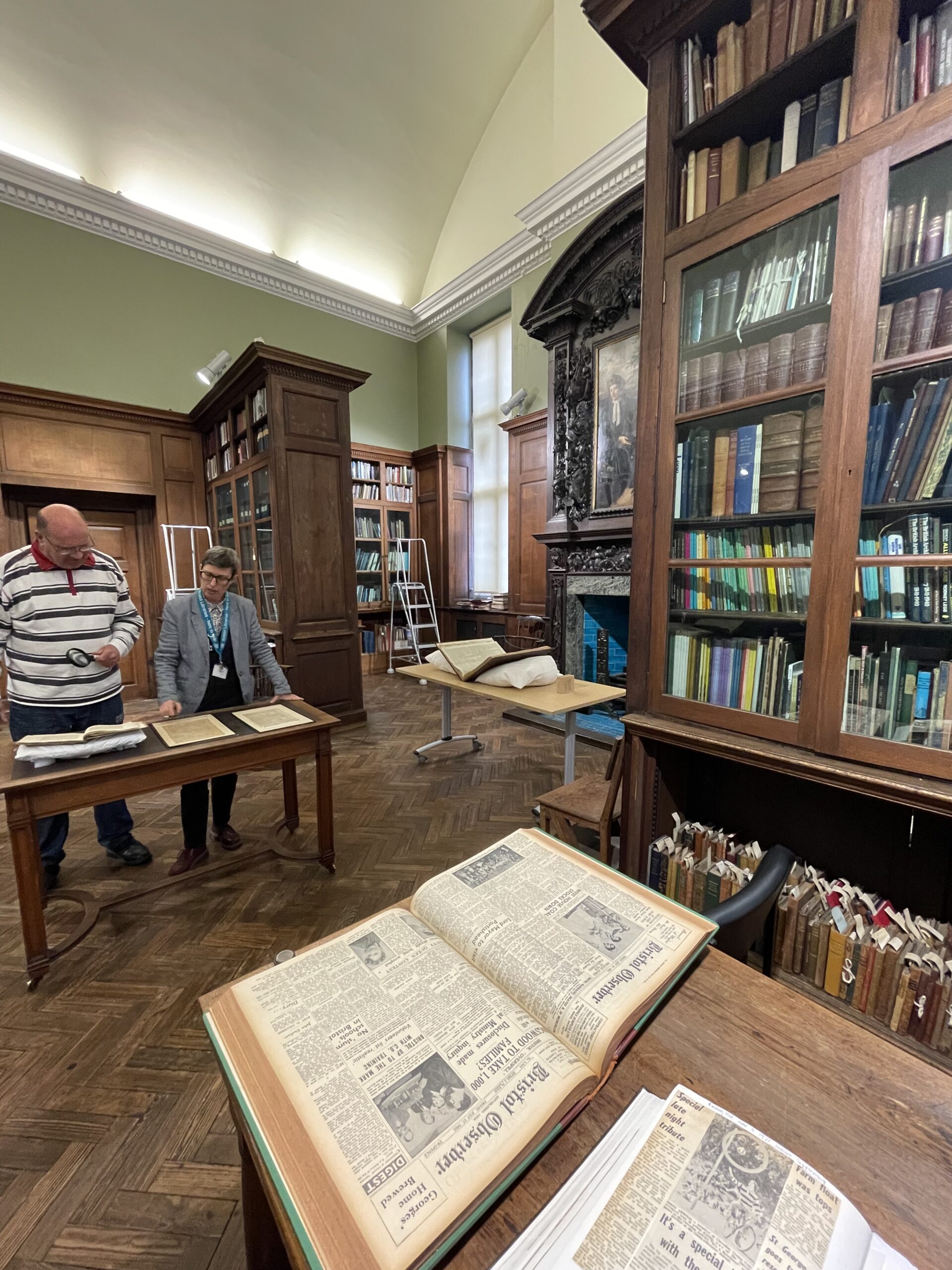 Old newspapers on tables with old books stored in glass cabinets and on shelves