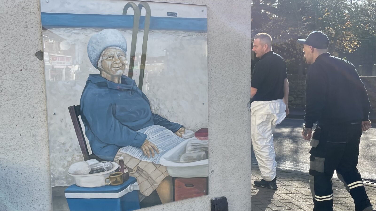 Two men walk by the mural of Lilian Rees, aka 'the 'cockle lady'