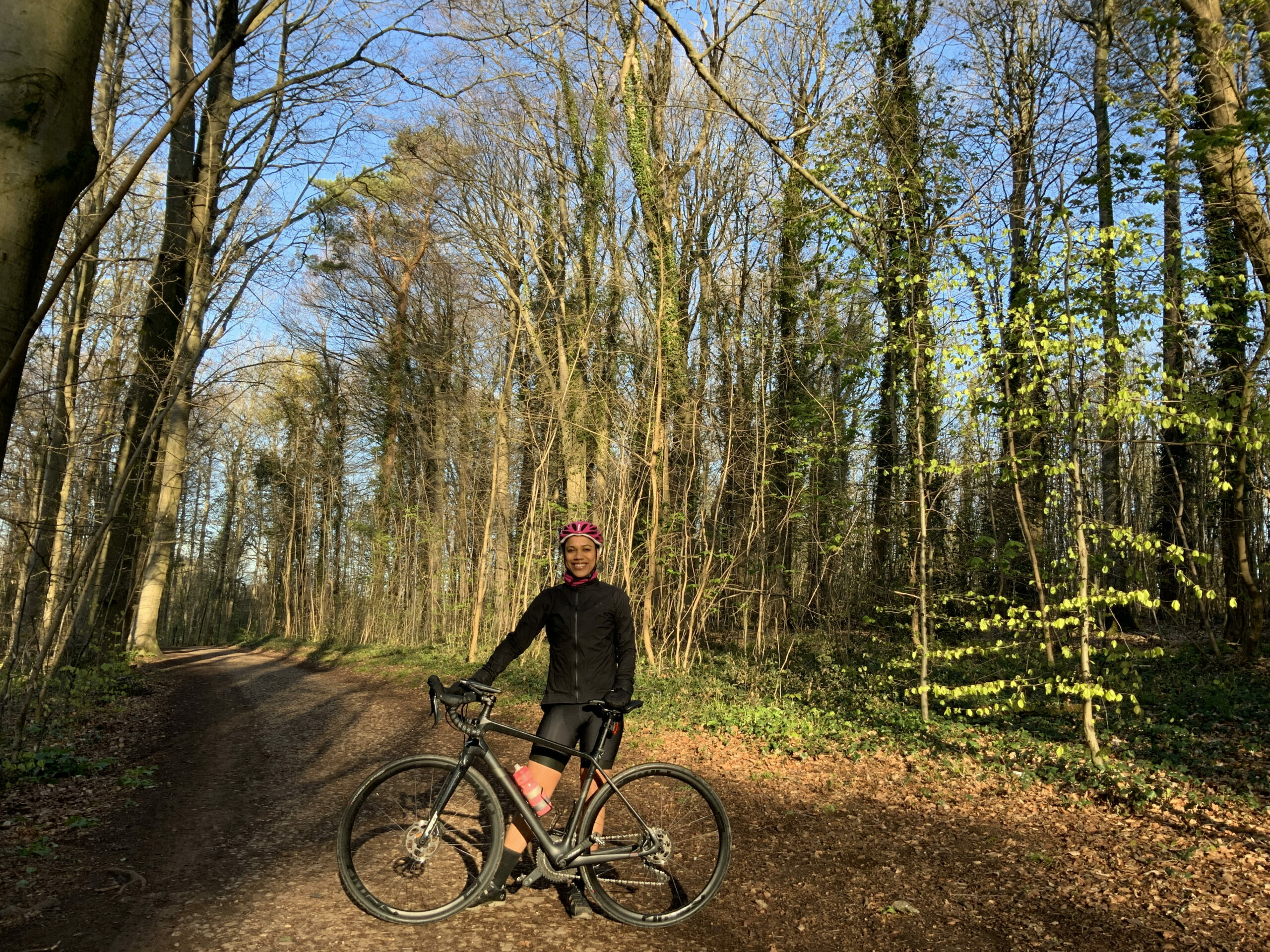 A woman stood in the middle of a woodland on a sunny day with her bicycle