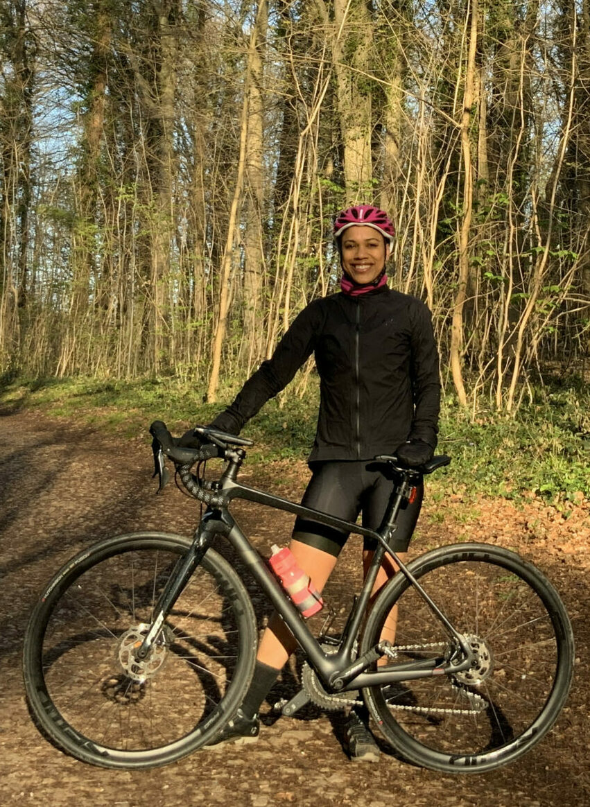 A woman stood in the middle of a woodland on a sunny day with her bicycle