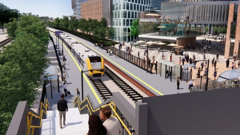 CGI of train pulling into station with people on the platforms, buildings in the background and a bridge in the foreground