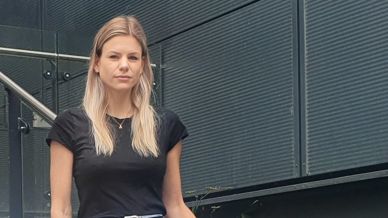 Blonde woman in her twenties wearing a black t-shirt and jeans looking unhappy in front of tall residential building