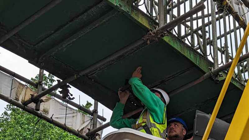 Two men inspect the green underside of an iron footbridge