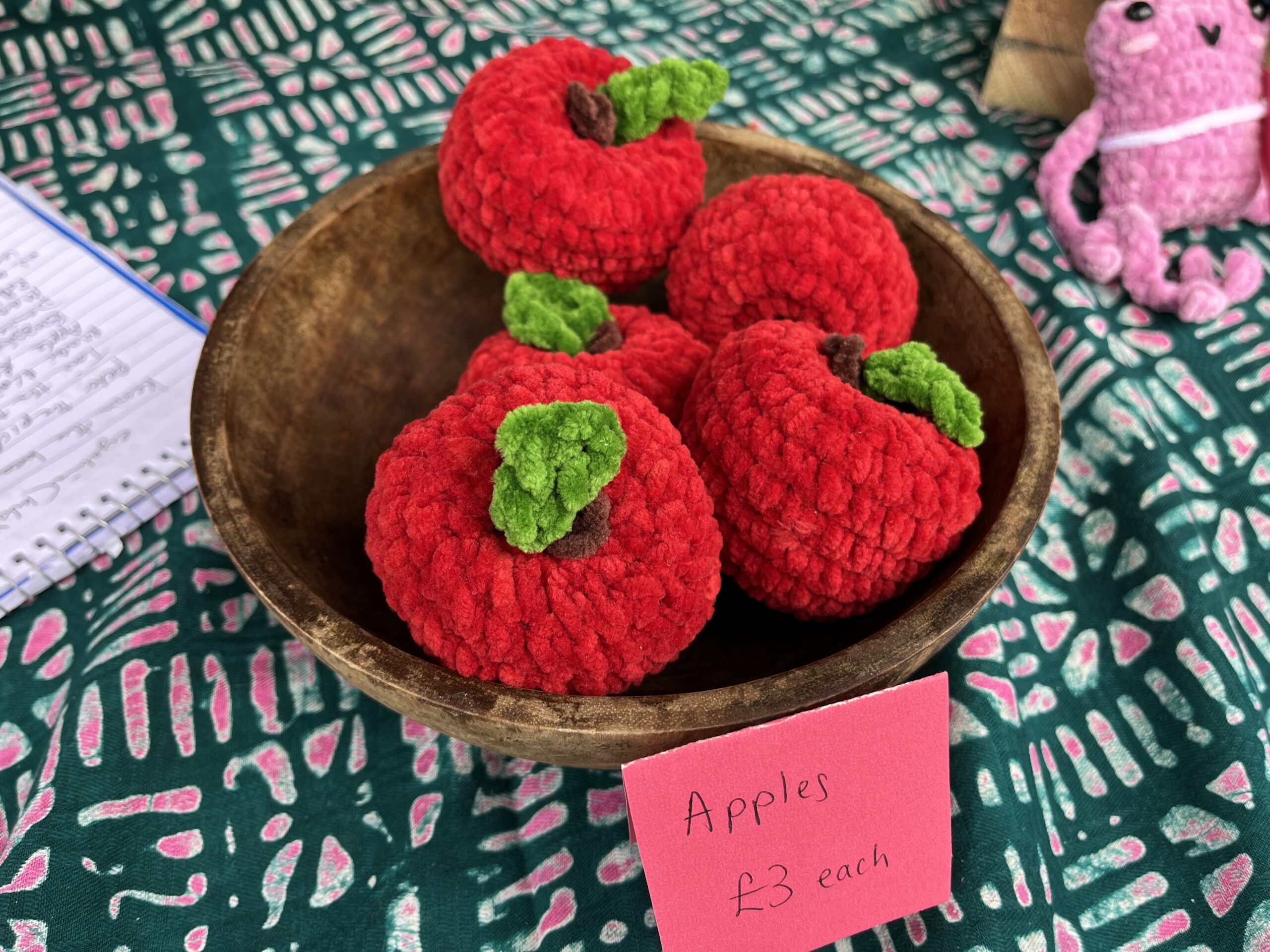 A wooden bowl containing bright red crocheted apples