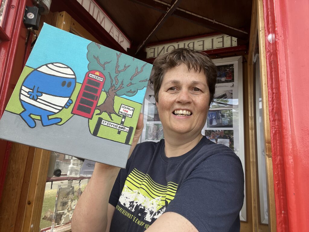 A women holds a small painting of Mr Bump depicted outside a phone box