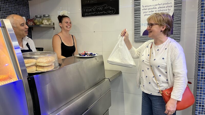 A lady collects a plastic bag of takeaway from a fish and chip counter