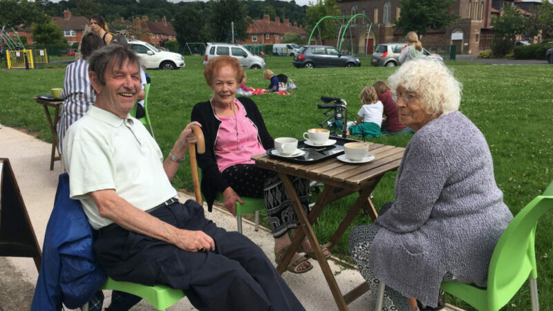 Three older people sit at an outside cafe table