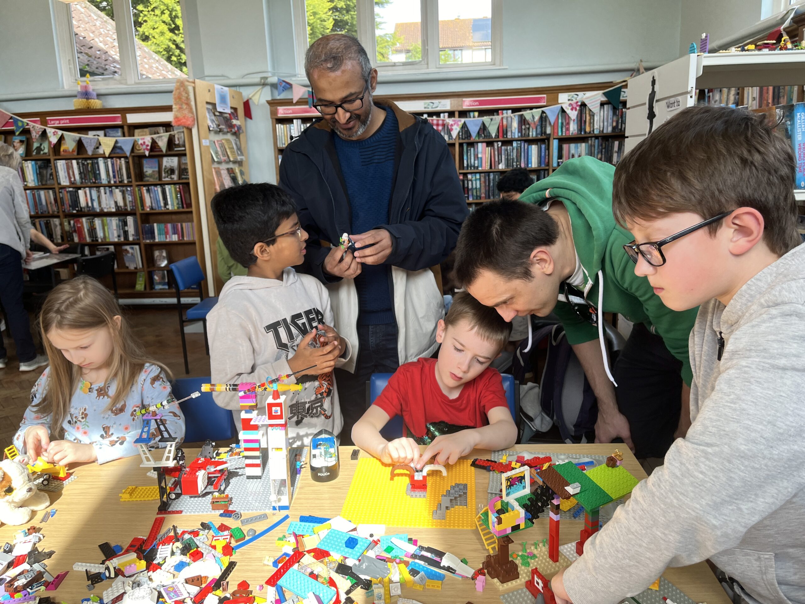 A group of children and adults make lego models. A pile of colourful lego is in front of them