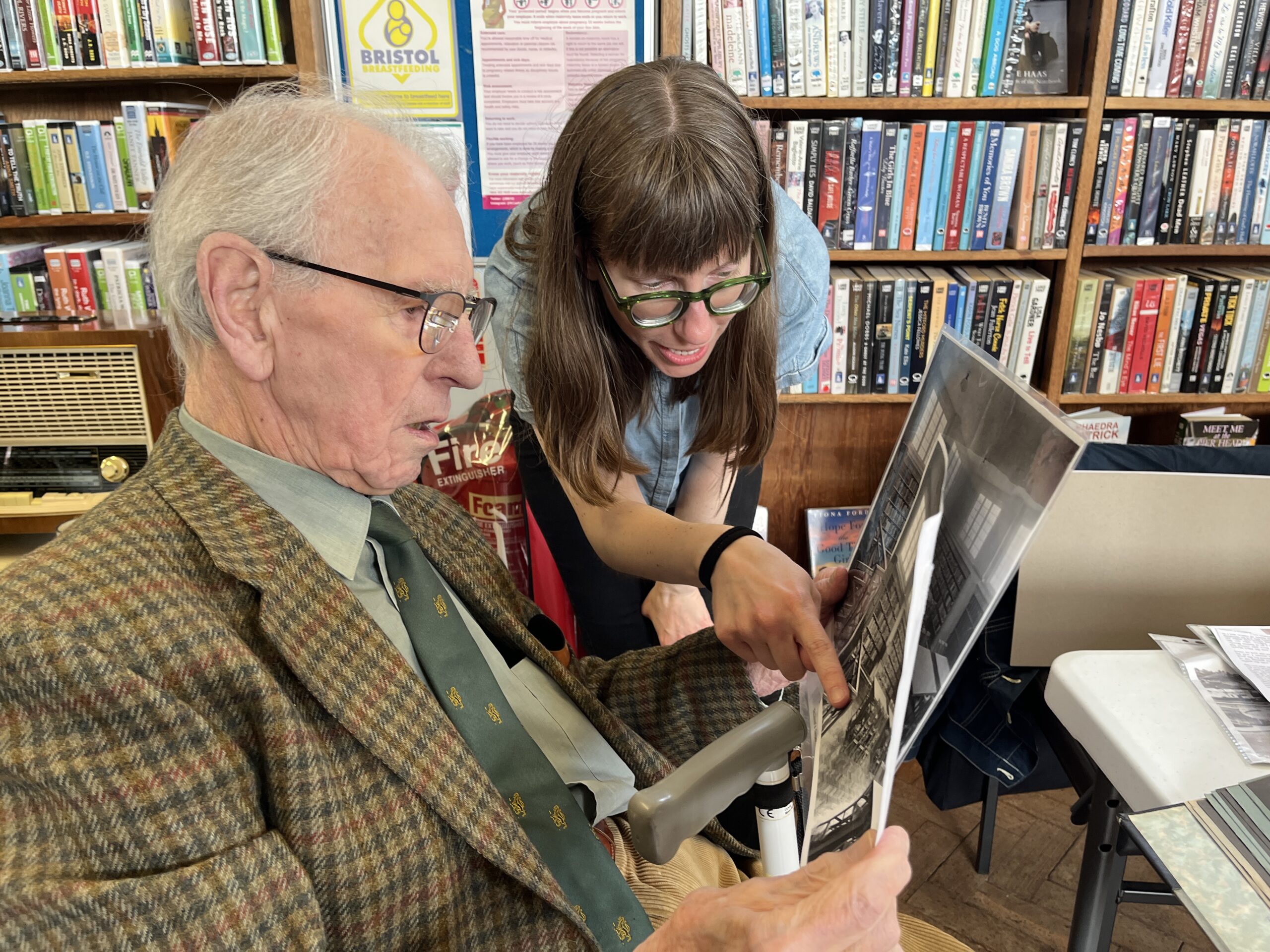 An oler man and a young women look at black a white photographs. There are books in the background