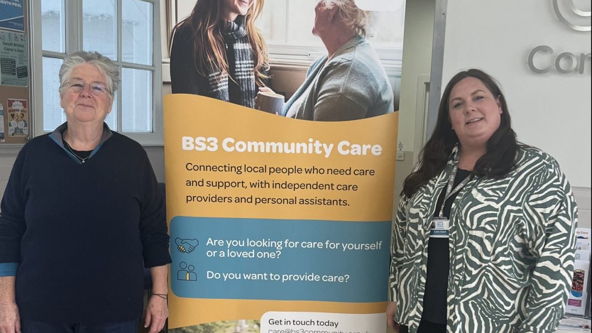 Syl and Carla stand next to a banner outlining BS£ community care's ideals