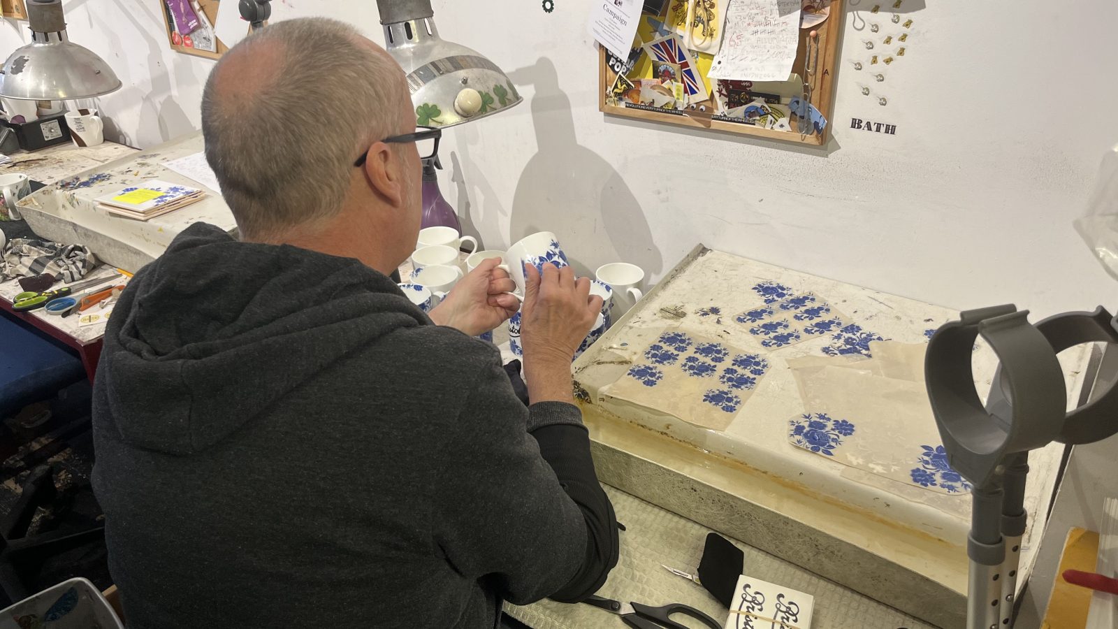 A man applies a thin decorative transfer to a ceramic mug in a workshop