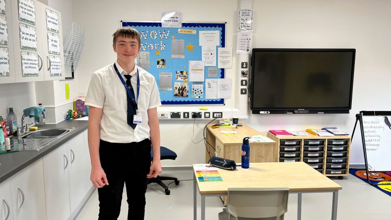 A young man stands in a brand new, tidy school classroom