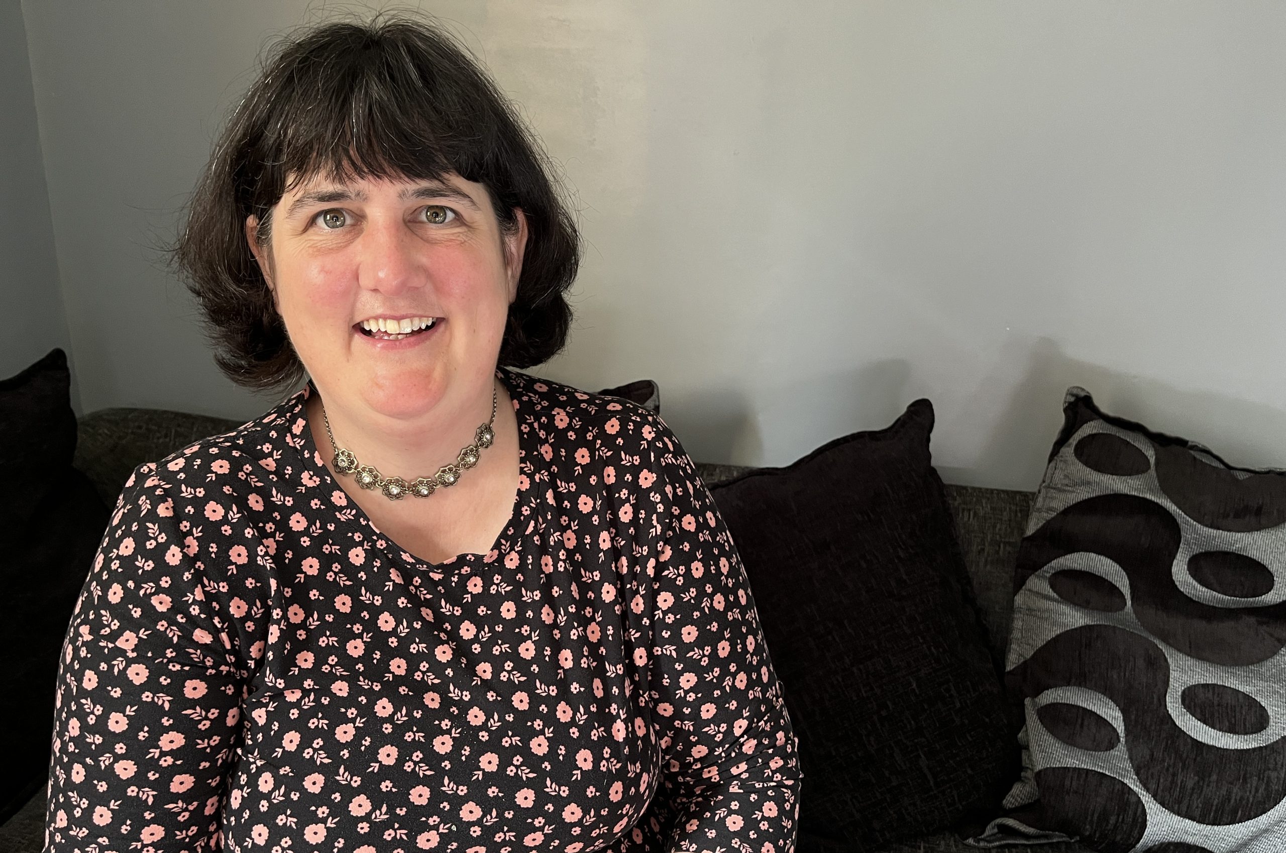 A young dark haired women sits smiling on a sofa