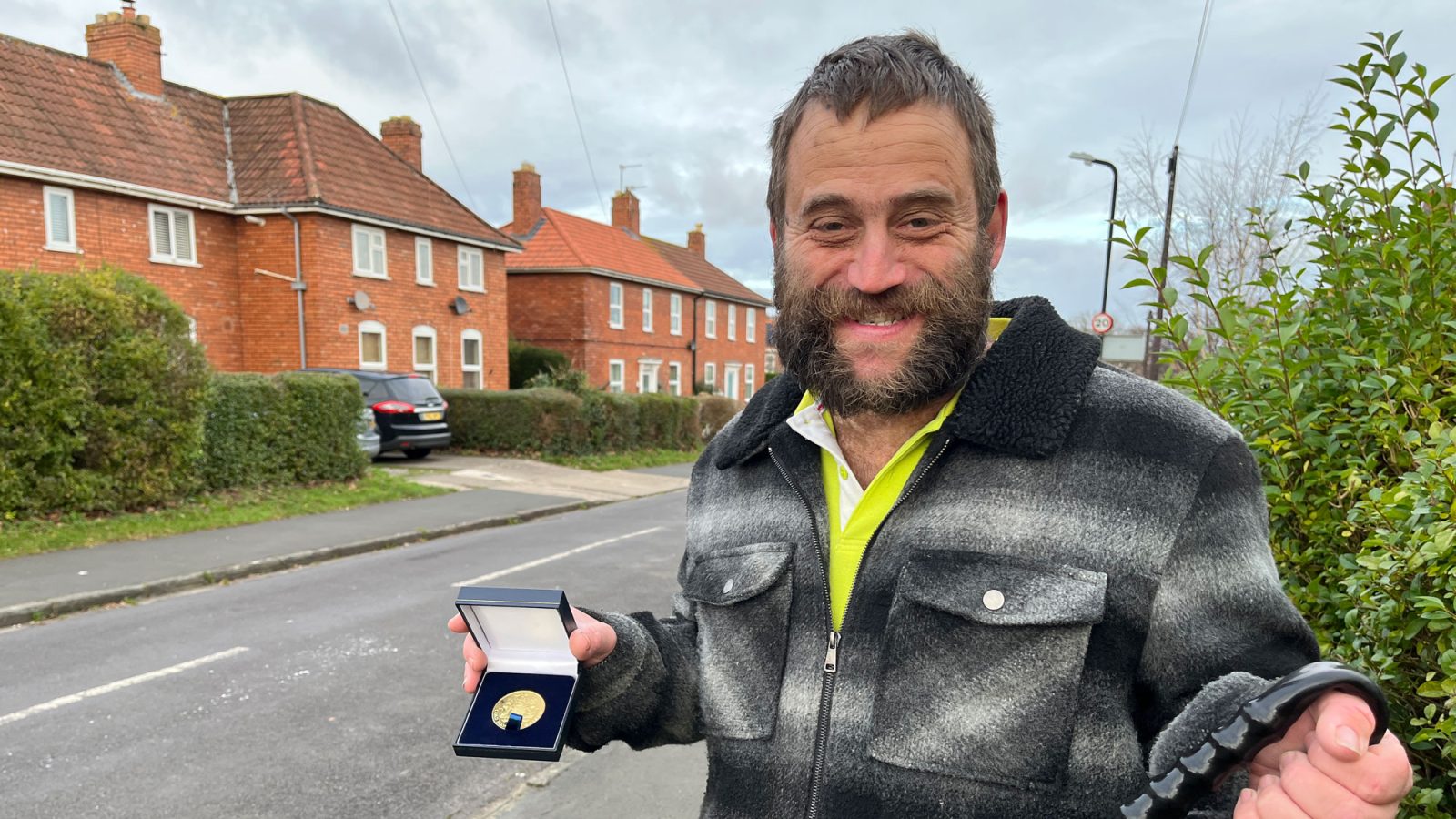 A man stands in the street holding a medal and a litter picker.