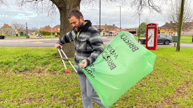 A man puts litter into a large green bag which is billowing in the wind