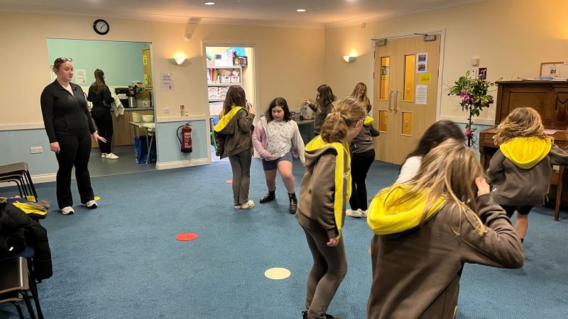 Girls run around in a small hall. Spots are placed on the carpet.