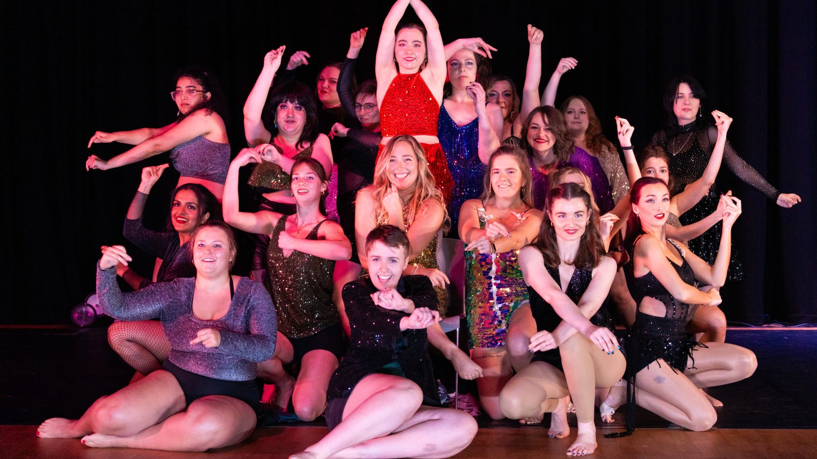 a group of smiling dancers pose on stage