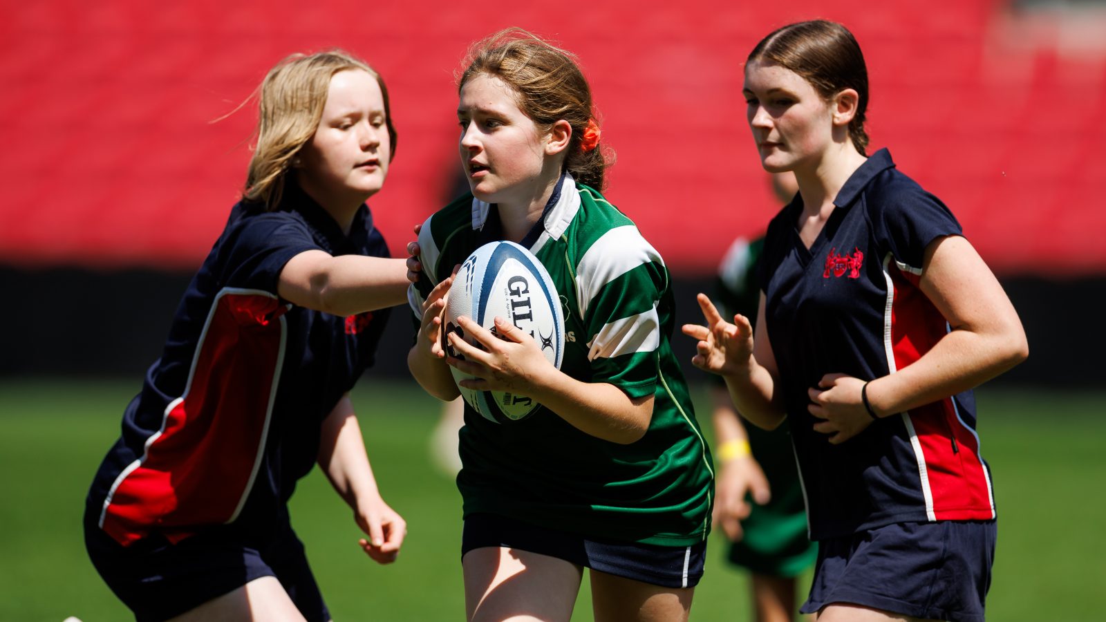 Three children playing rugby. The middle child is holding a rugby ball.
