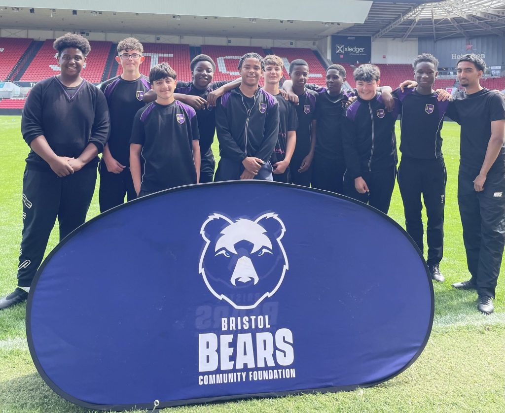 A group of boys in sports kit pose behind a 'Bristol Bears Community Foundation' sign