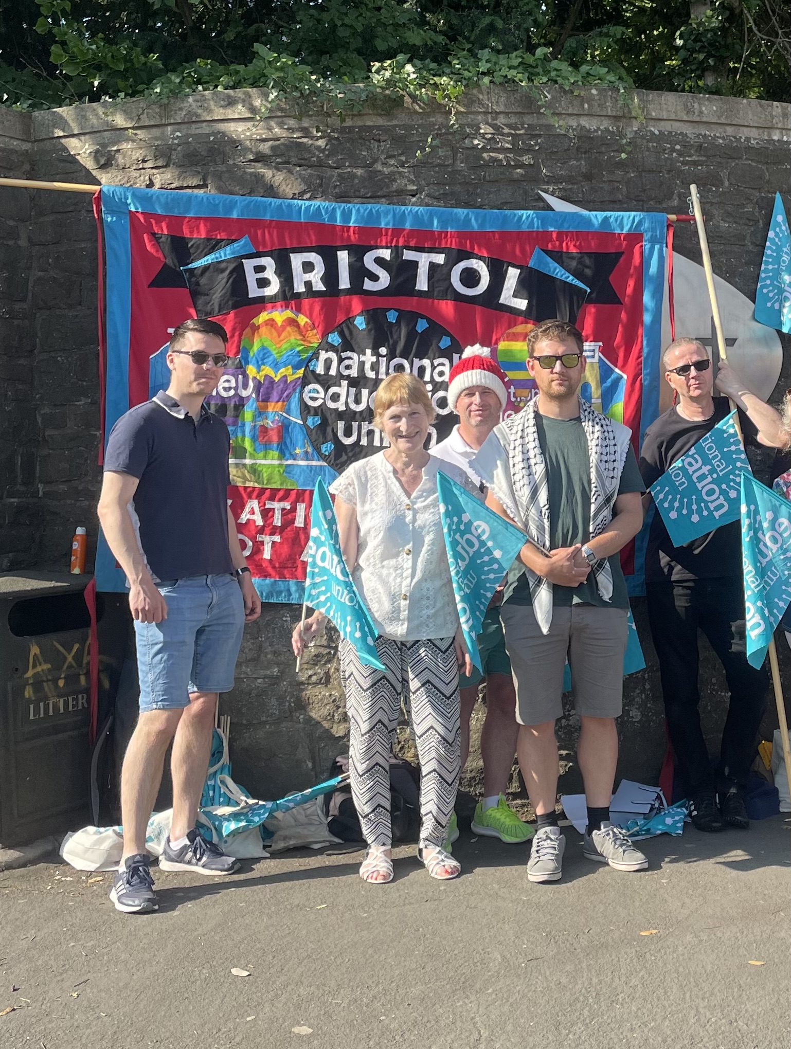 Teachers holding National Education Union flags stand in front of a vibrant banner