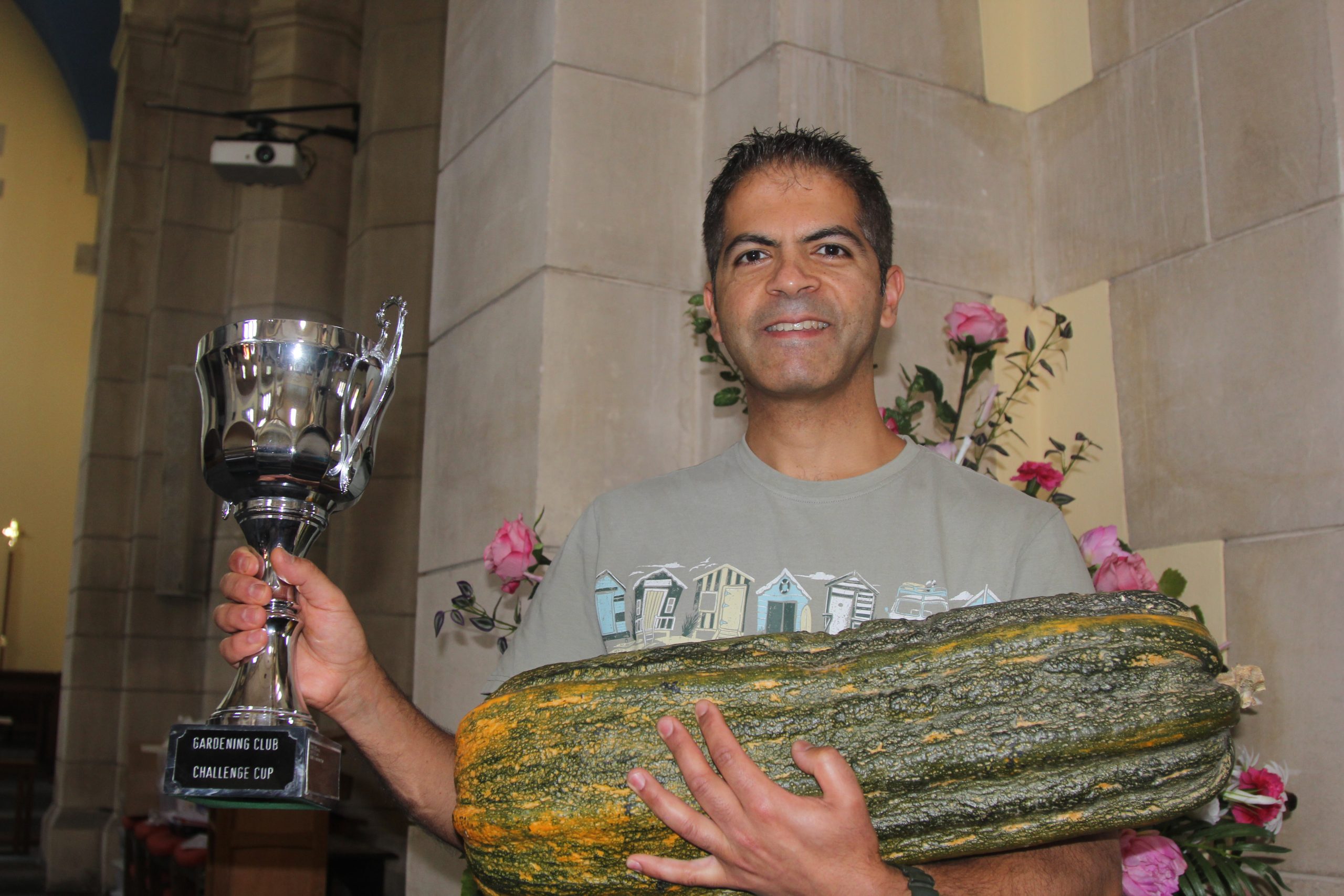 A man holds a silver cup and a giant marrow