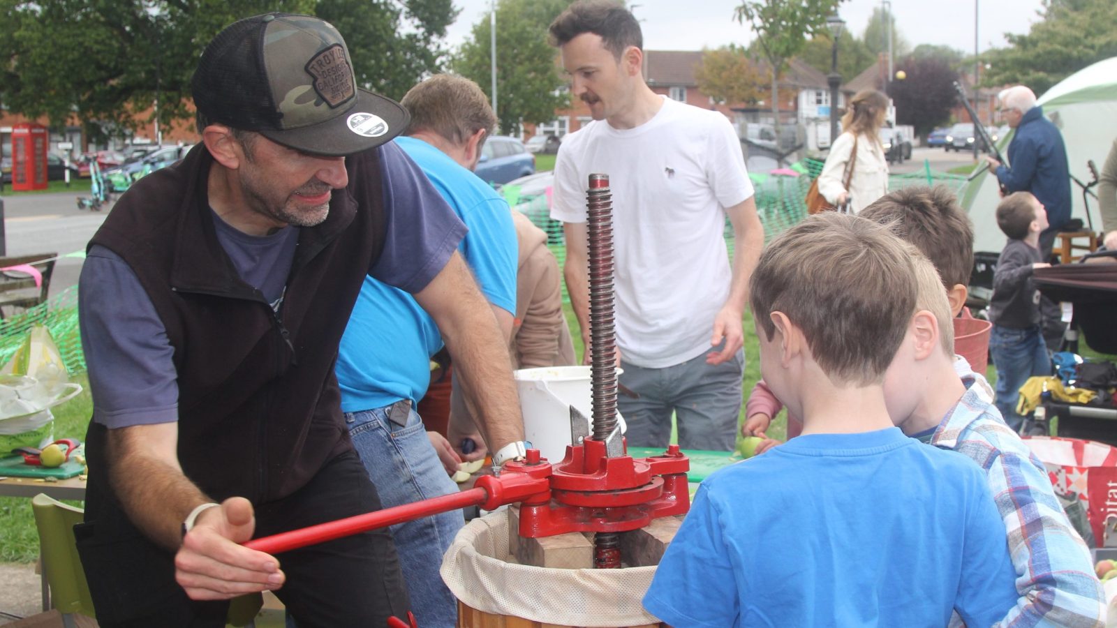 A man uses a hand apple press as children watch