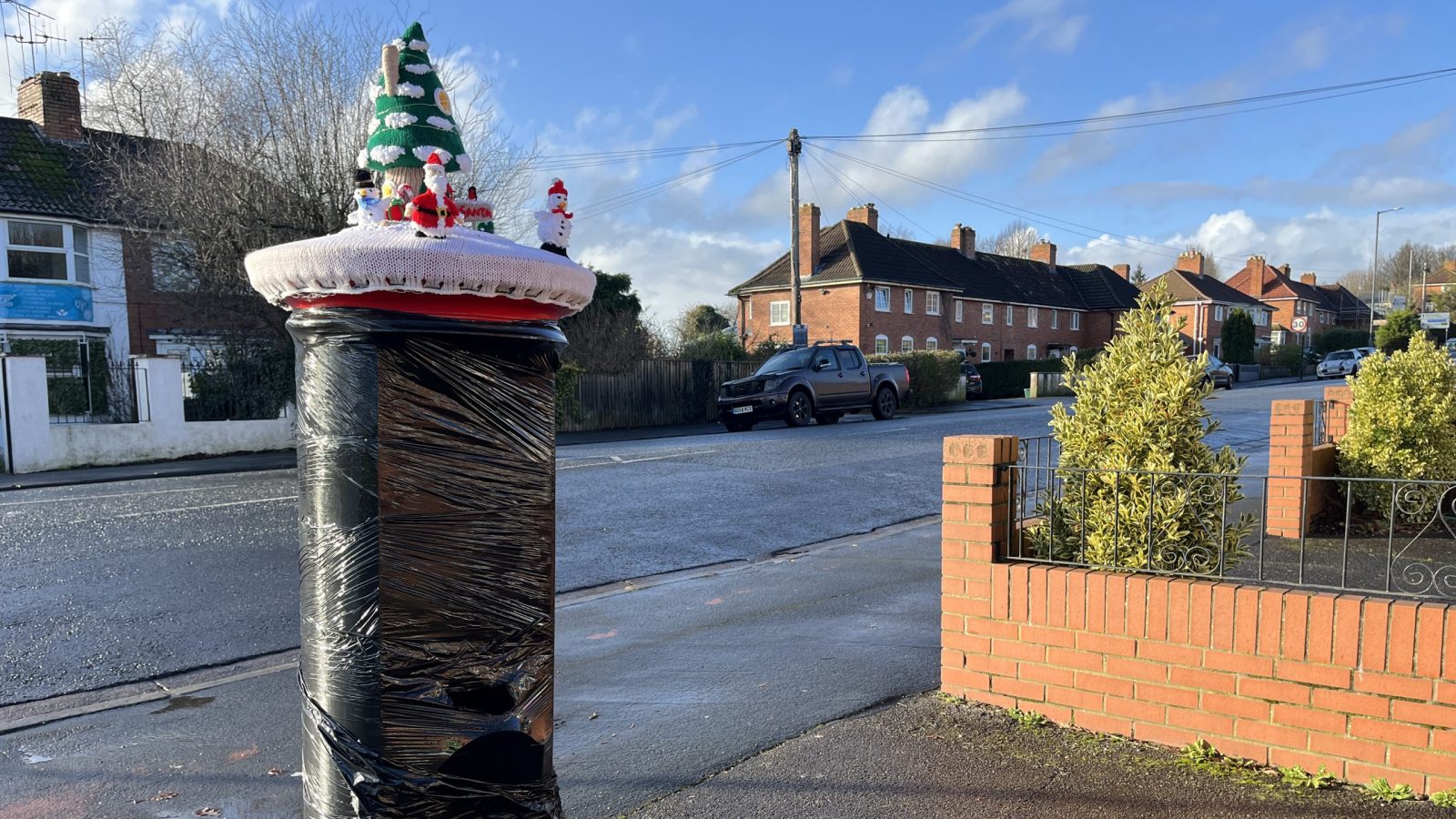 Post box wrapper in black plastic with a knitted topper on it